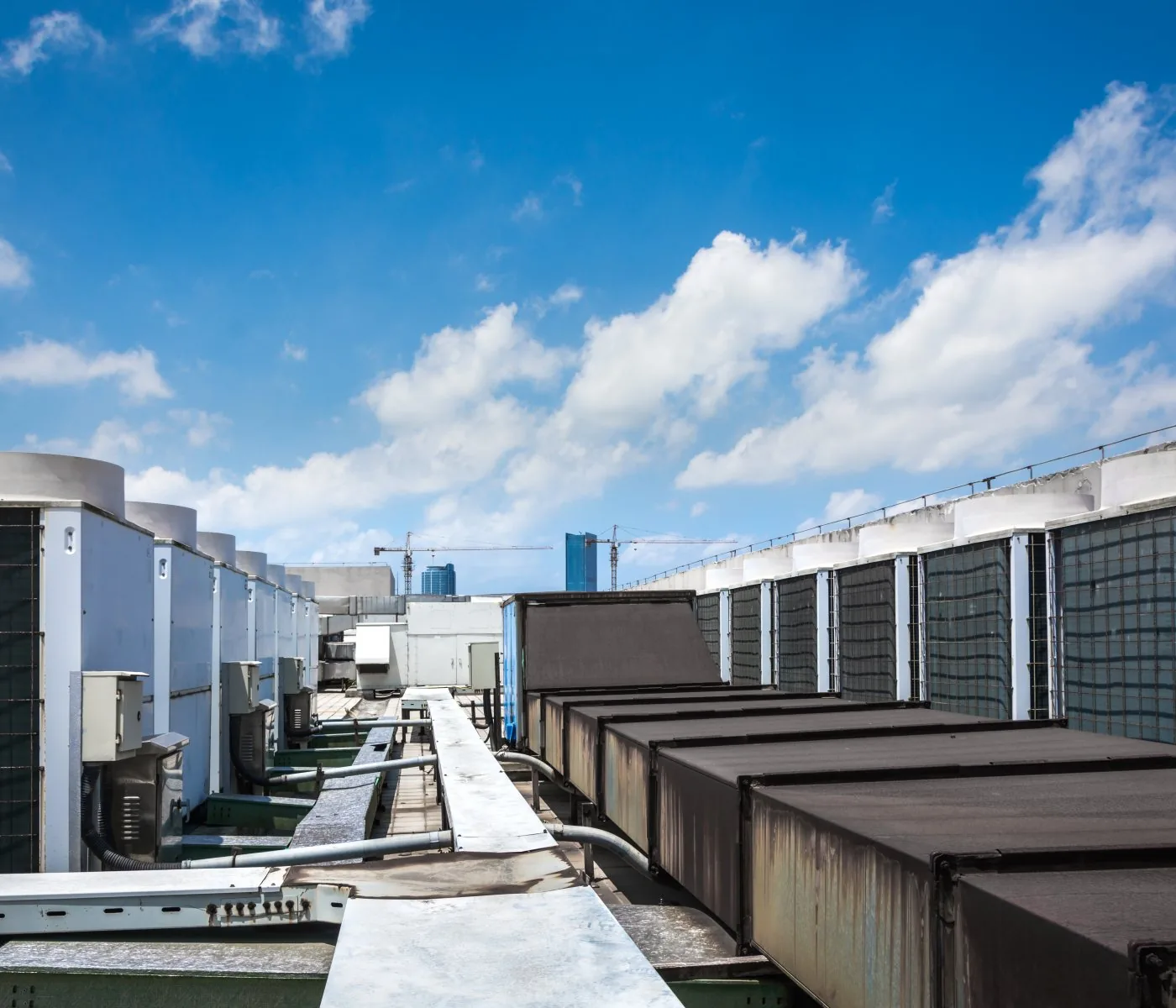 Rows of commercial air conditioning units on a building rooftop under a blue sky