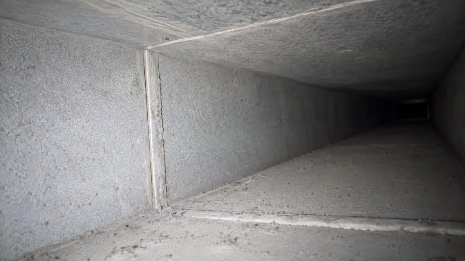 The inside of a residential sheet-metal air duct showing a light, even coating of household dust