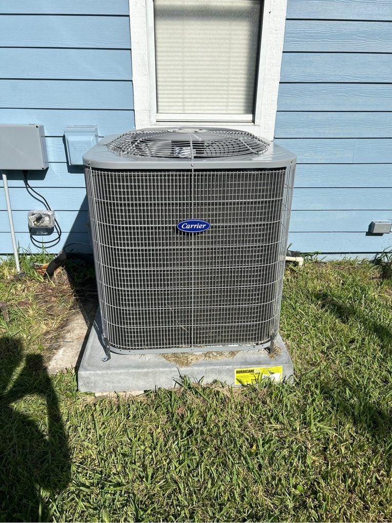 A new Carrier air conditioner condenser on a concrete pad beside a blue-sided Jacksonville home, with a hurricane tie-down tag on the slab