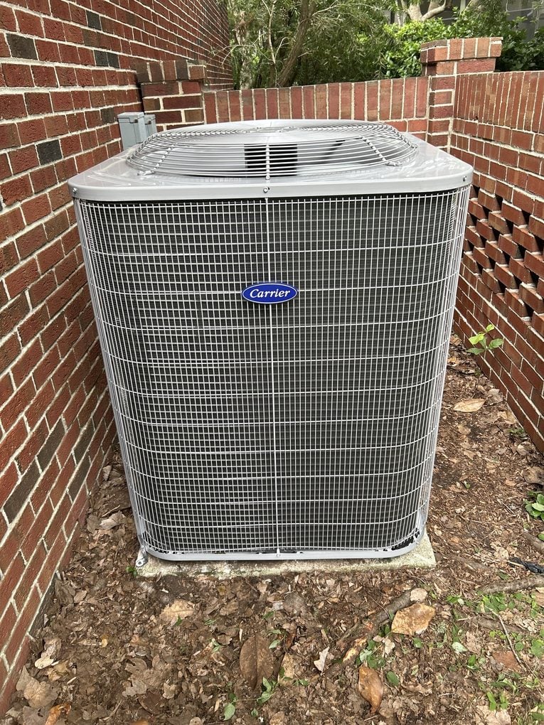 A new Carrier condenser installed on a pad in a brick courtyard alcove at a Jacksonville home