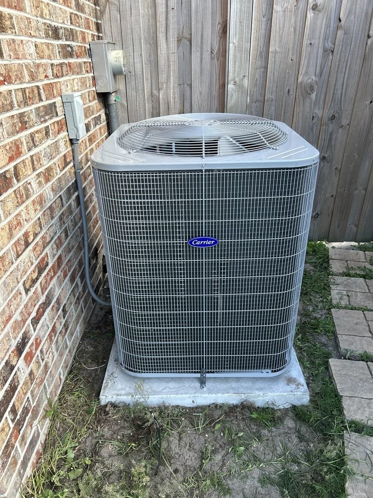 A new Carrier condenser on a concrete pad between a brick wall and a wood fence at a Jacksonville home