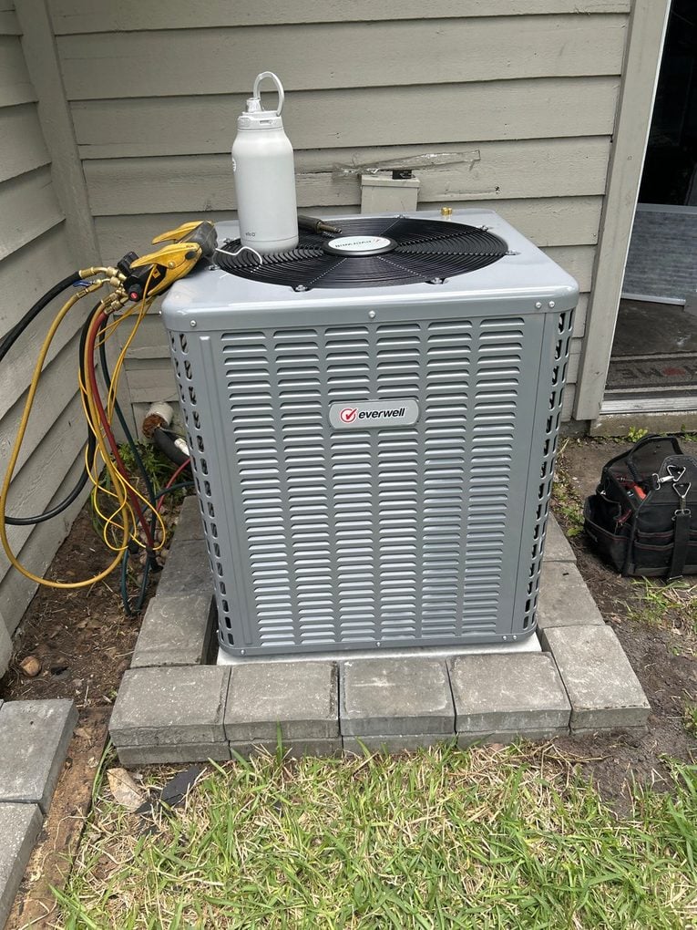 A newly installed outdoor condenser sitting level on a paver pad with manifold gauges connected during the refrigerant charge