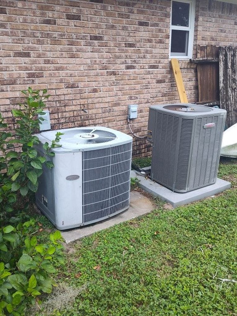 Two outdoor condensing units side by side on pads along the back of a brick Jacksonville home