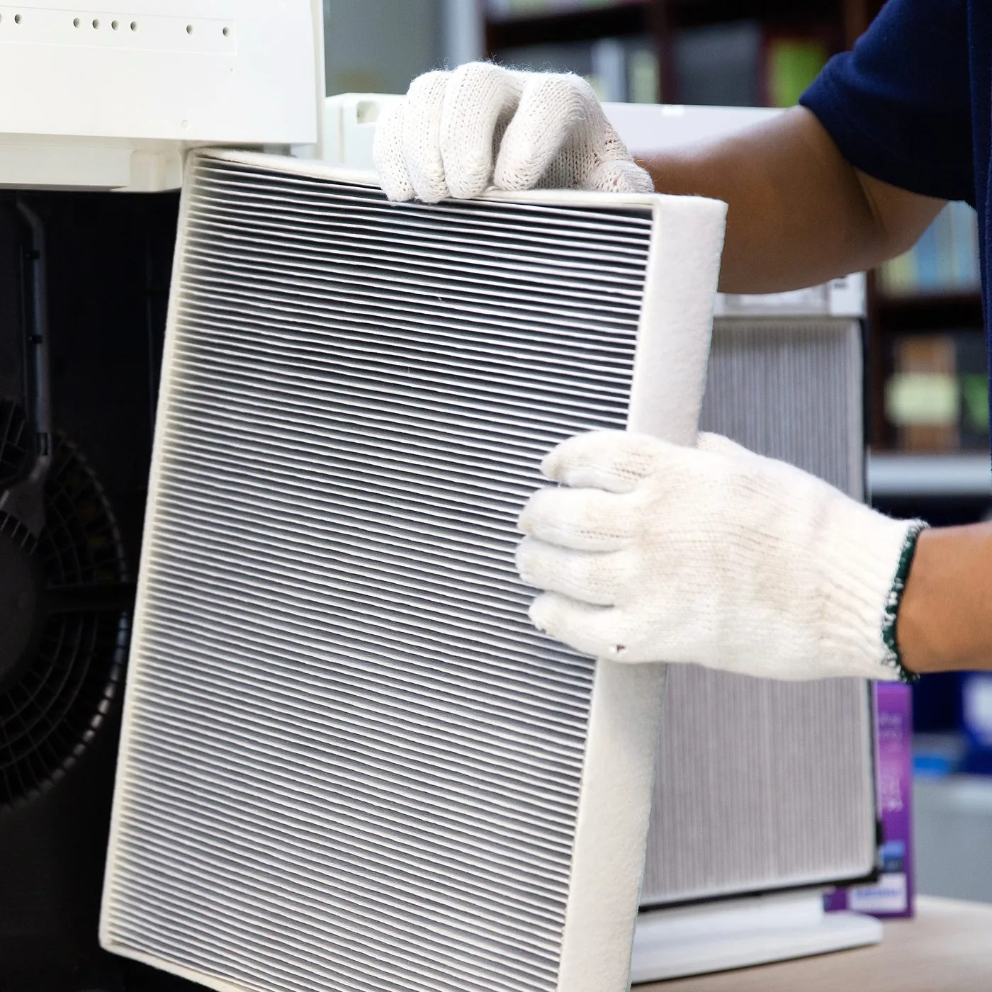 A gloved technician sliding a dust-loaded pleated filter out of an air cleaner